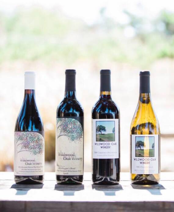 Four bottles of Wildwood Oak Winery wine displayed outdoors with vineyard rows softly blurred in the background.